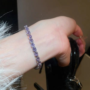 Close-up of sparkling purple zircon tennis bracelet worn on a white knit sweater cuff