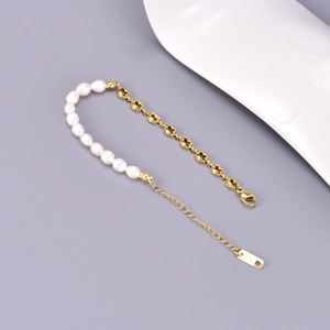 Macro shot of asymmetric bracelet with white freshwater pearls and golden coffee bean chain