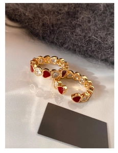 Detail of gold-plated open rings with red enamel hearts and sparkling crystal accents