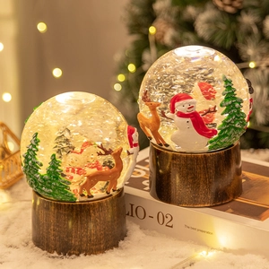 Boule à neige de Noël lumineuse avec Père Noël et renne sur un socle en bois