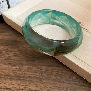 Close-up of green resin bangle with brown marble texture on a neutral display tray