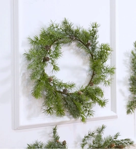 Detail of a green pine needle Christmas wreath with natural pinecones on a white wall