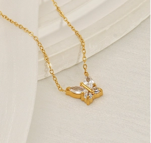 Detail of a gold butterfly necklace with zircon stones on a white textured background