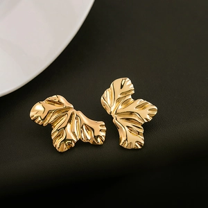 Minimalist gold leaf earrings featuring irregular metal textures on black leather surface
