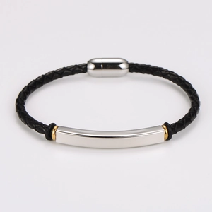 Detail of woven black leather bracelet with silver curved plate and gold metal accents