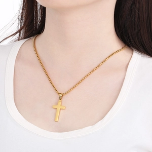 Close-up of a polished gold cross pendant with a box chain worn by a model