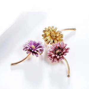 Three minimalist daisy brooches in purple, yellow, and red with long golden stems