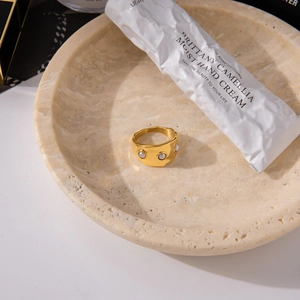 Detail of wide gold titanium ring with three faux pearls on beige marble tray
