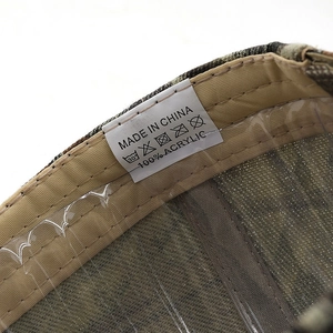 Détail macro d'une casquette camouflage montrant le tissu acrylique et l'étiquette de soin