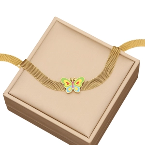 Parure collier en maille dorée avec papillon en émail coloré sur un coffret à bijoux beige