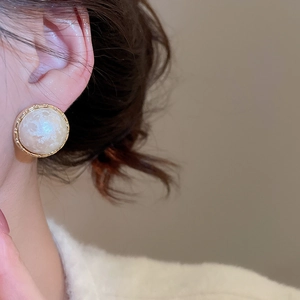 Detail of round gold-plated earrings with white marbled texture on model's ear