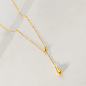 Detailed view of gold titanium steel Y-shaped necklace with teardrop pendants on white blocks
