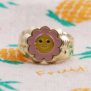 Detail of gold flower ring featuring pink enamel petals and a yellow smiley face