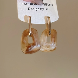Detailed macro of amber marbled acrylic square earrings hanging on golden metal bars