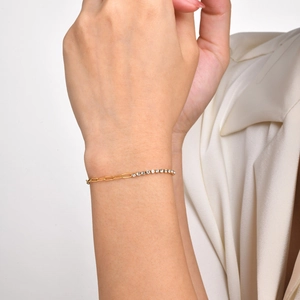 Detailed shot of a gold paperclip chain bracelet with white cubic zirconia on a model's wrist