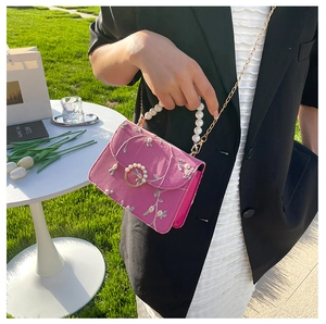 Close-up of pink embroidered small square bag with pearl handle and metal chain