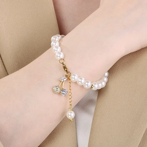 Close-up of pearl bracelet with diamond cherry pendant worn on wrist over a beige blazer