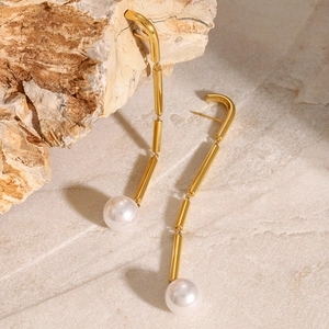 Macro detail of gold tassel drop earrings with white pearls on a textured stone base