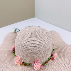 Close-up of woven straw sun hat with decorative pink roses and green leaves