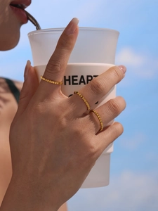 Detailed view of three golden gear-textured stainless steel rings worn by a model