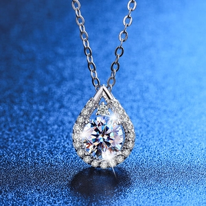 Dettaglio macro di una collana con ciondolo a goccia in argento e grande diamante su blu