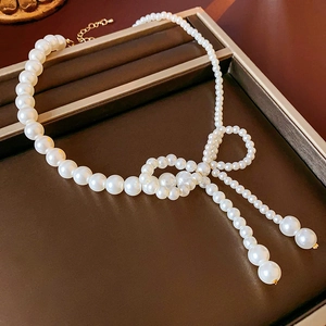 Dettaglio della collana di perle con chiusura a fiocco dorato su vassoio in pelle nera