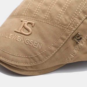 Detail of light brown cotton ivy cap featuring embroidered letters and metallic logo badge