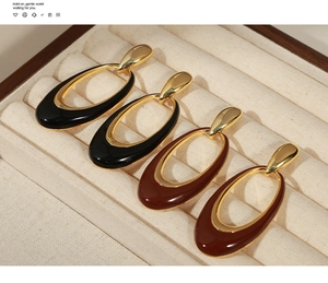 Detailed close-up of oval enamel drop earrings in black and brown on velvet display