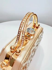 Detailed view of luxury gold clutch bag with sparkling rhinestones and pearl embellishments