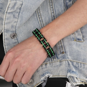 Close-up of black and green bicycle chain bracelet on male model wrist in denim jacket