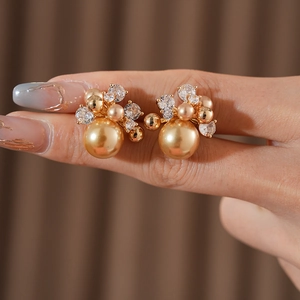 Detailed close-up of a gold pearl earring with clear crystals held by hand on brown cloth