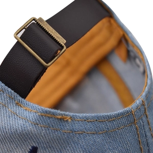 Dettaglio cappello baseball in denim blu con cinturino in pelle e fibbia in metallo