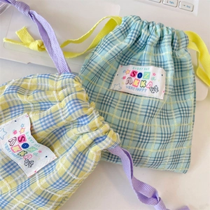 Close-up of colorful plaid drawstring storage bags with cute 'SOZ AKKA' label detail.