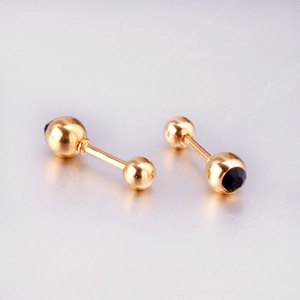 Detail of gold barbell earring with a round black zircon stone inlay on a metal surface