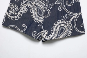 Detail of white paisley embroidery on dark blue denim fabric shorts for women