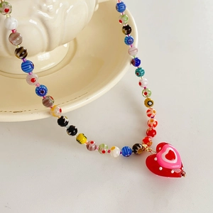 Macro shot of colorful handmade glass beads and a red heart pendant on a ceramic dish