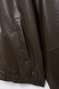 Detail view of deep brown faux leather jacket with pocket and elastic hem texture