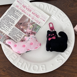 Detail of cute plush cat keychains in pink and black on a vintage porcelain dish
