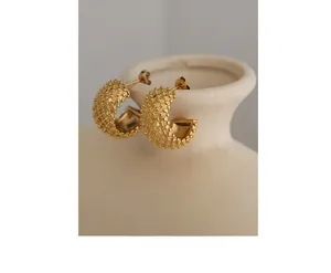 Detailed view of gold C-shaped earrings with bead texture on a ceramic vase
