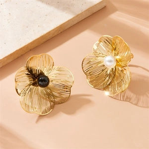Golden flower earrings with black and white beads on a stone background