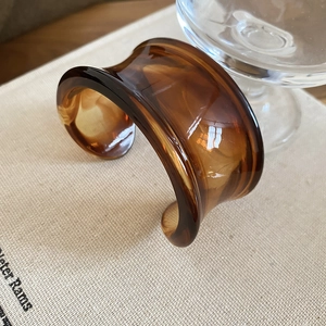 Detail of a brown amber resin cuff bracelet with translucent wavy patterns and wide curve