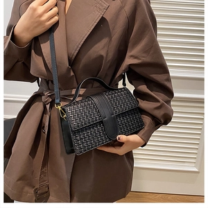 Close-up of black woven texture handbag with gold buckle on a brown trench coat