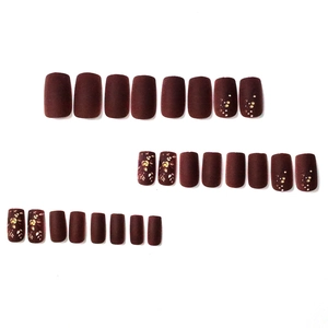Faux ongles bordeaux mats avec motifs floraux dorés et pois sur fond blanc épuré