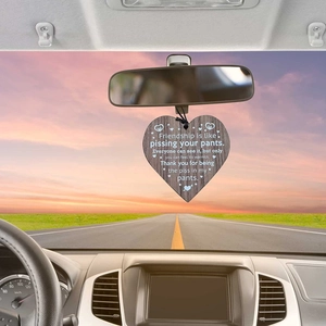 Wooden heart-shaped friendship pendant hanging on a car rearview mirror over a sunset road