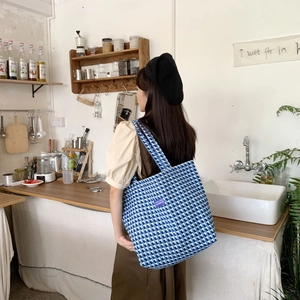 Close-up of blue and white plaid canvas tote bag worn by a model in a cafe setting