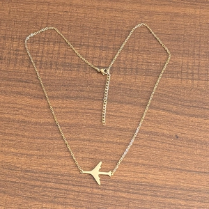 Détail du collier avec pendentif avion plaqué or 18 carats et chaîne réglable sur bois
