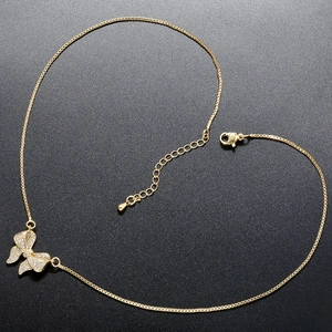Detailed view of a gold bow pendant necklace with sparkling white zircons on black surface