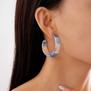 Close-up of bohemian C-shaped earrings with colorful woven rope texture on a model