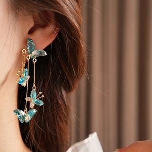 Gros plan d'un mannequin portant des boucles d'oreilles papillon dorées et cristaux bleus