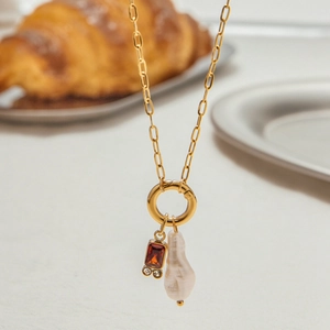 Detail of golden paperclip chain necklace with baroque pearl and orange gemstone charm